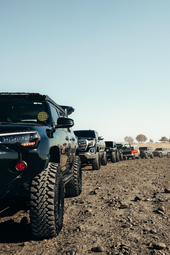A lineup of modified offroad trucks on a gravel plain