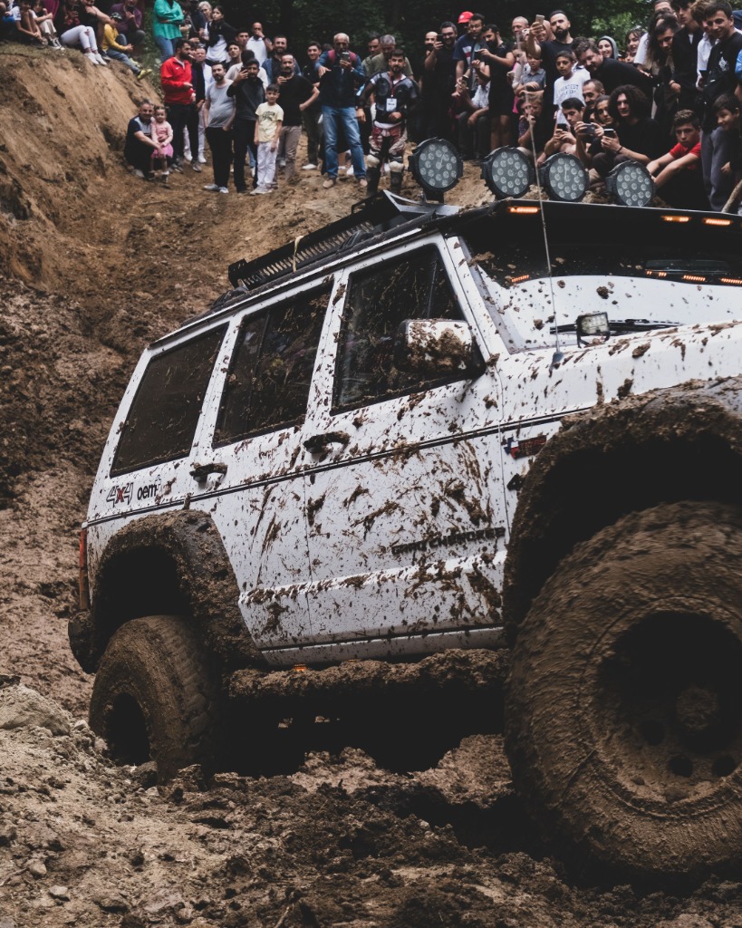 Offroad jeep conquering a mud hill with a crowd watching